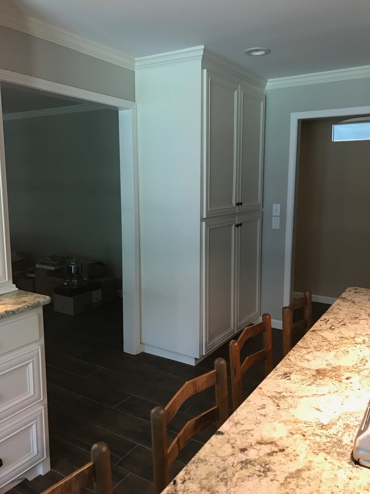 Eat-in kitchen - large transitional l-shaped brown floor eat-in kitchen idea in Birmingham with a farmhouse sink, recessed-panel cabinets, white cabinets, beige backsplash, stainless steel appliances and an island