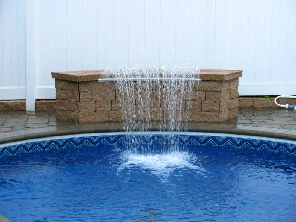 Photo of a large traditional backyard round pool in New York with a water feature.