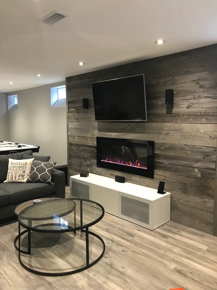Design ideas for a mid-sized contemporary fully buried basement in Toronto with grey walls, laminate floors, a standard fireplace, a wood fireplace surround and grey floor.