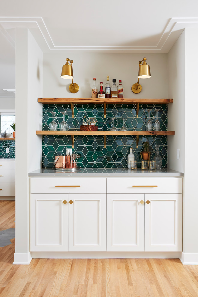 This is an example of a transitional single-wall home bar in Minneapolis with white cabinets, ceramic splashback, no sink, recessed-panel cabinets, green splashback, light hardwood floors, beige floor and grey benchtop.