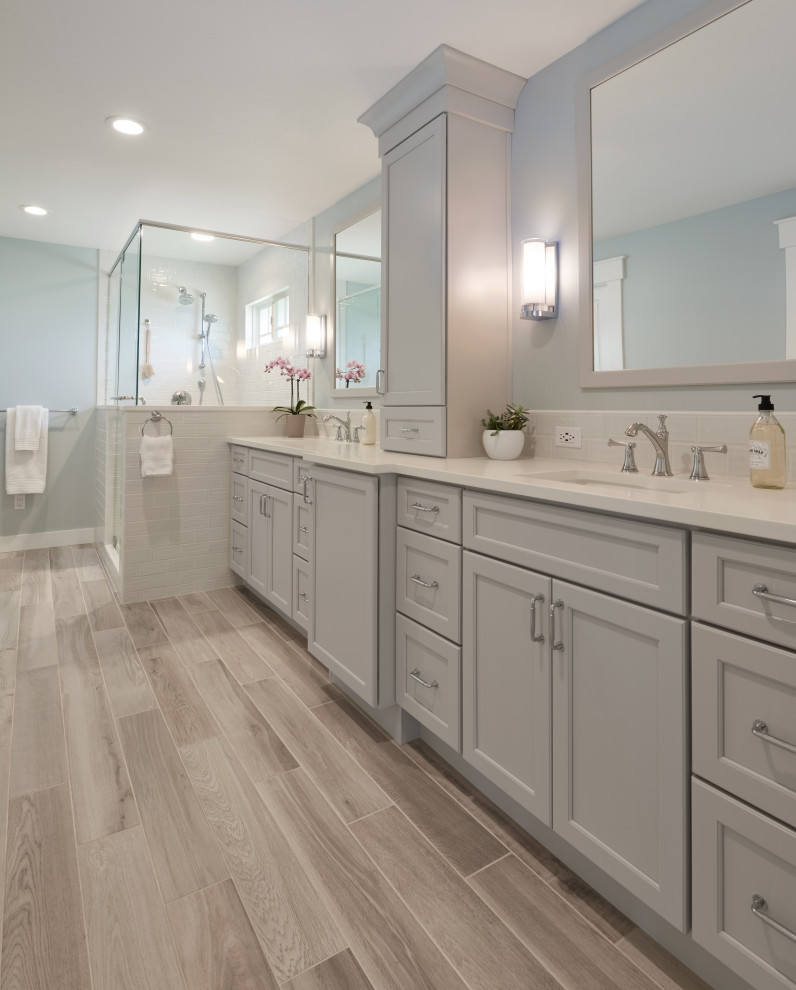 Design ideas for a large beach style master bathroom in Seattle with shaker cabinets, grey cabinets, a one-piece toilet, white tile, ceramic tile, blue walls, porcelain floors, an undermount sink, engineered quartz benchtops, brown floor, a hinged shower door and white benchtops.