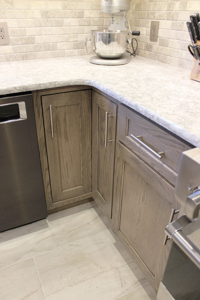 This is an example of a mid-sized traditional u-shaped eat-in kitchen in Other with an undermount sink, flat-panel cabinets, grey cabinets, quartz benchtops, grey splashback, limestone splashback, stainless steel appliances, ceramic floors, with island, grey floor and grey benchtop.