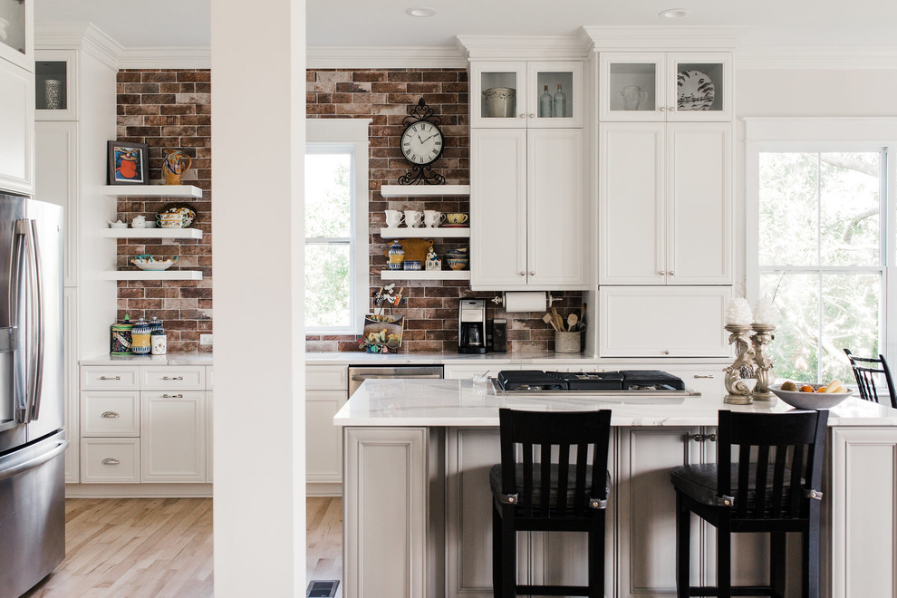 Mid-sized transitional u-shaped eat-in kitchen in Charleston with white cabinets, brick splashback, with island, an undermount sink, shaker cabinets, quartz benchtops, red splashback, stainless steel appliances, light hardwood floors, beige floor and white benchtop.