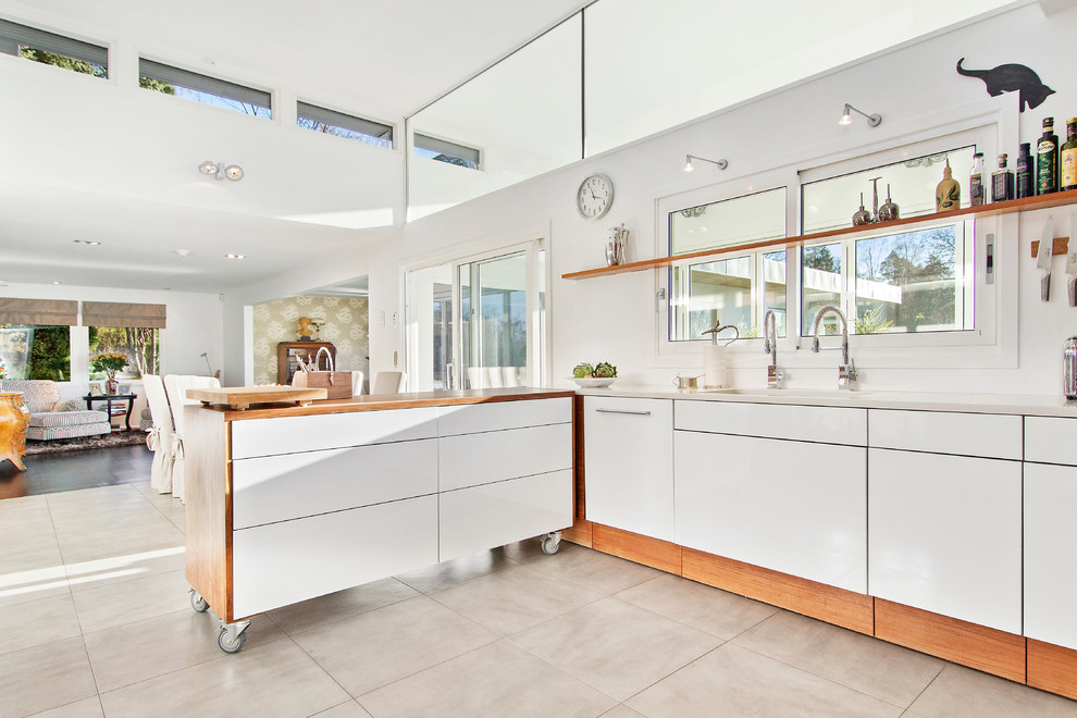 Large contemporary l-shaped kitchen in Stockholm with flat-panel cabinets, white cabinets, a peninsula, a double-bowl sink, wood benchtops, white appliances and limestone floors.
