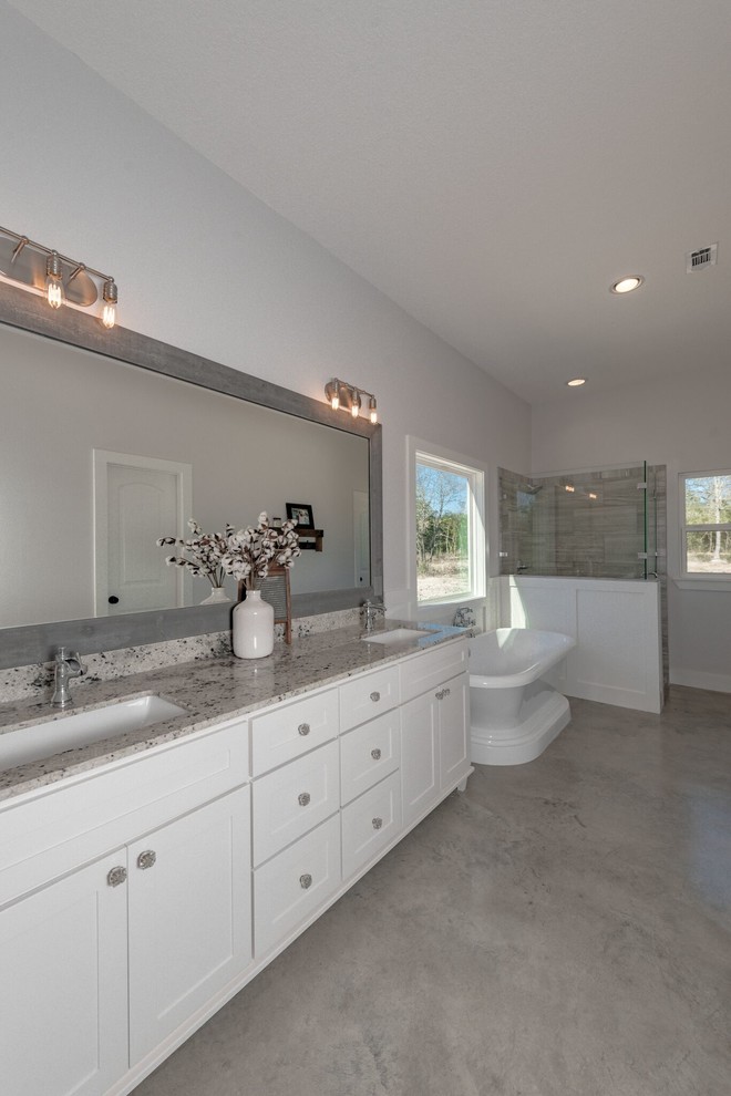 Inspiration for a mid-sized country master bathroom in Austin with shaker cabinets, white cabinets, a freestanding tub, an open shower, a two-piece toilet, gray tile, stone tile, white walls, concrete floors, an undermount sink, granite benchtops, grey floor and an open shower.