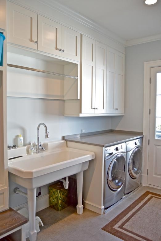Design ideas for a mid-sized traditional utility room in Chicago with an utility sink, shaker cabinets, white cabinets, solid surface benchtops, grey walls, limestone floors and a side-by-side washer and dryer.