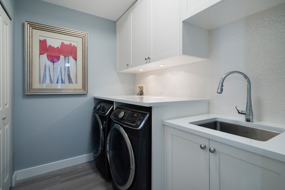 This is an example of a mid-sized transitional single-wall dedicated laundry room in Vancouver with an undermount sink, recessed-panel cabinets, white cabinets, quartz benchtops, blue walls, porcelain floors and a side-by-side washer and dryer.