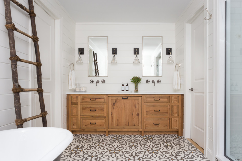 Photo of a country bathroom in New York with shaker cabinets, medium wood cabinets, a freestanding tub and white walls.