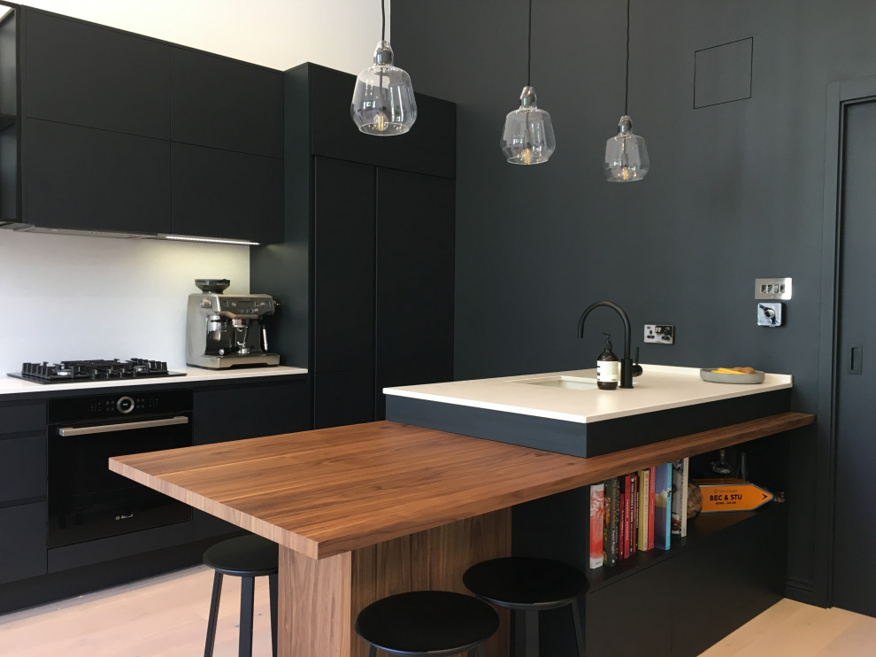 Photo of a small contemporary galley open plan kitchen in London with flat-panel cabinets, black cabinets, quartzite benchtops, white splashback, with island and white benchtop.