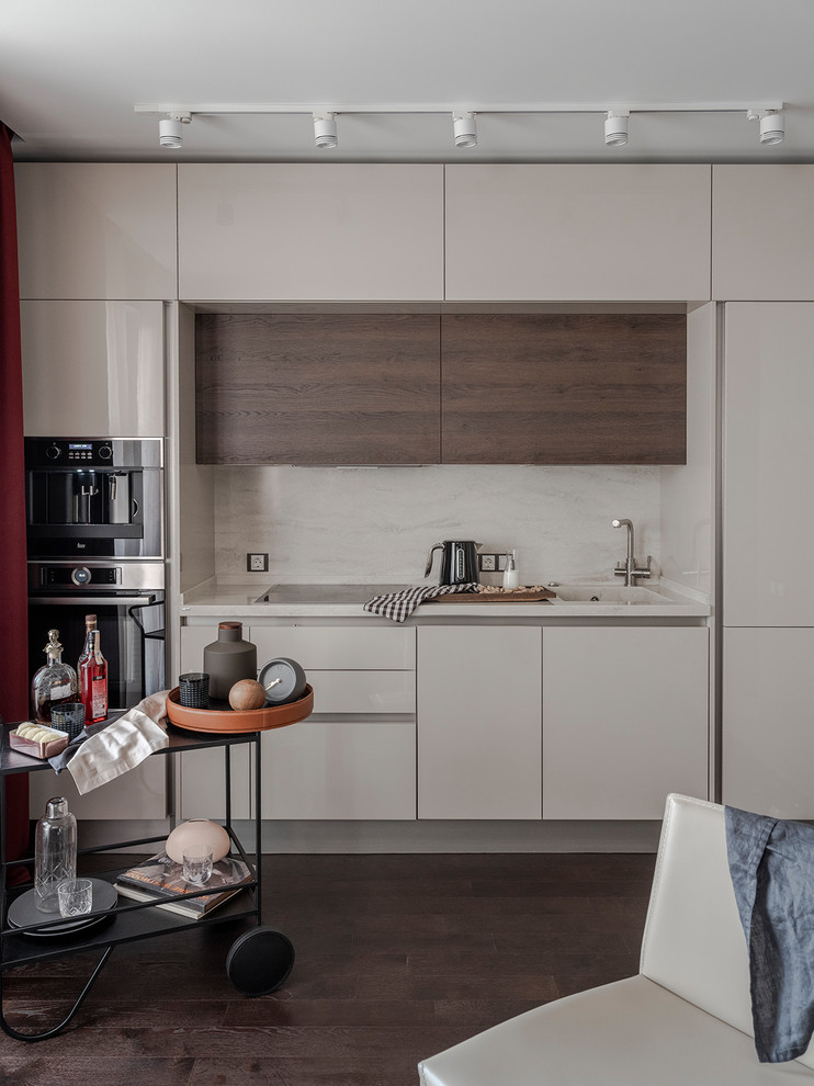 Small contemporary single-wall open plan kitchen in Moscow with an integrated sink, flat-panel cabinets, beige cabinets, beige splashback, no island, brown floor, beige benchtop, stone slab splashback, black appliances and dark hardwood floors.