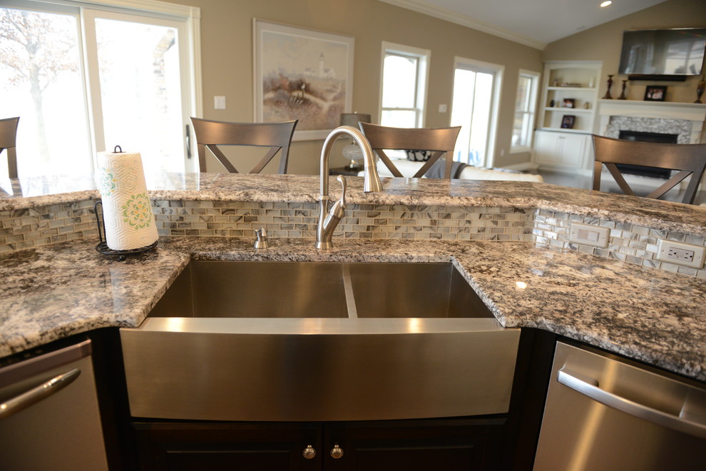 Inspiration for a huge transitional l-shaped medium tone wood floor eat-in kitchen remodel in Chicago with a farmhouse sink, raised-panel cabinets, white cabinets, granite countertops, beige backsplash, stone tile backsplash, stainless steel appliances and an island