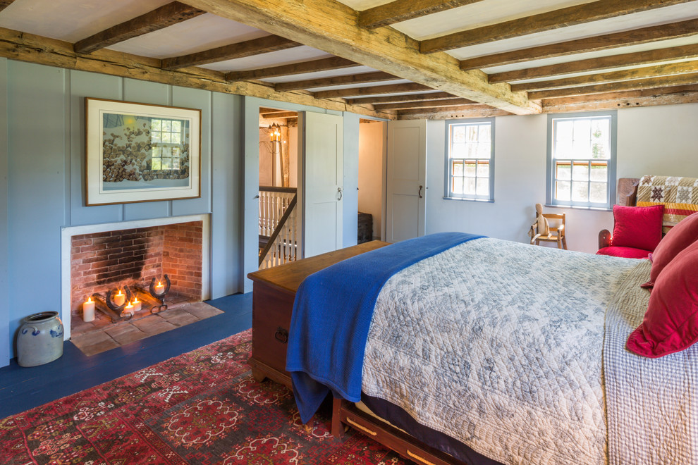 Country master bedroom in Boston with blue walls, painted wood floors, a standard fireplace and a wood fireplace surround.
