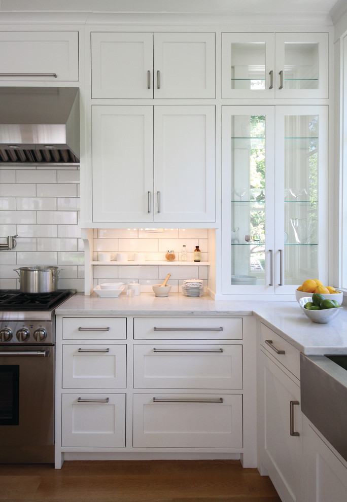 Design ideas for a large traditional u-shaped kitchen in Minneapolis with stainless steel appliances, medium hardwood floors, with island, quartz benchtops, a farmhouse sink, recessed-panel cabinets, white cabinets, white splashback and subway tile splashback.