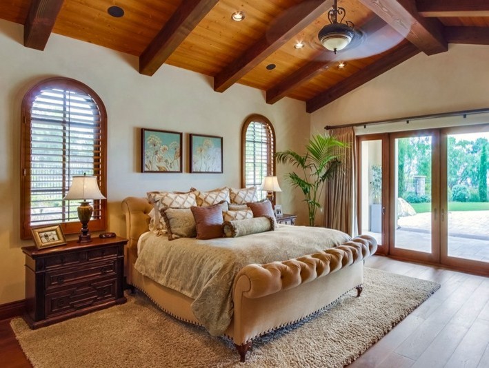 Design ideas for an expansive mediterranean master bedroom in San Diego with beige walls, dark hardwood floors, a standard fireplace, a stone fireplace surround and brown floor.