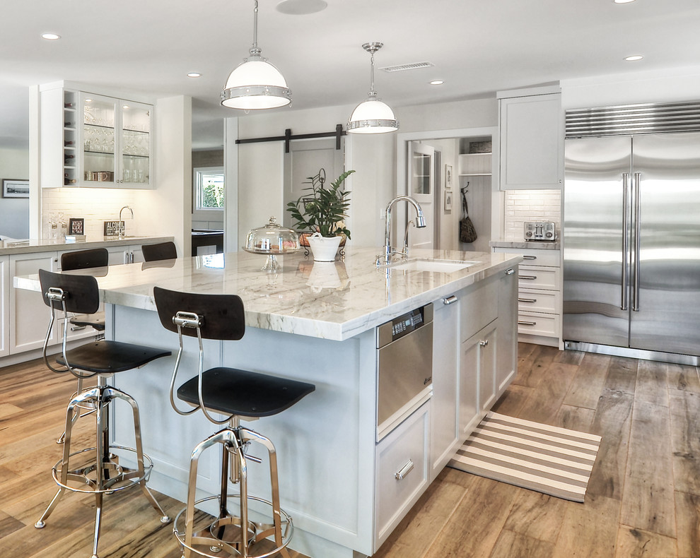 Mid-sized transitional l-shaped medium tone wood floor and brown floor kitchen pantry photo in Orange County with an undermount sink, recessed-panel cabinets, white cabinets, white backsplash, stainless steel appliances, an island, subway tile backsplash, quartzite countertops and white countertops