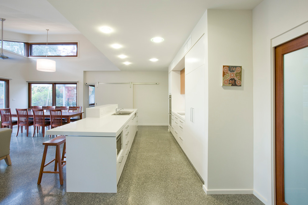 Large contemporary galley open plan kitchen in Canberra - Queanbeyan with a double-bowl sink, white cabinets, quartz benchtops, white splashback, stainless steel appliances, concrete floors and with island.