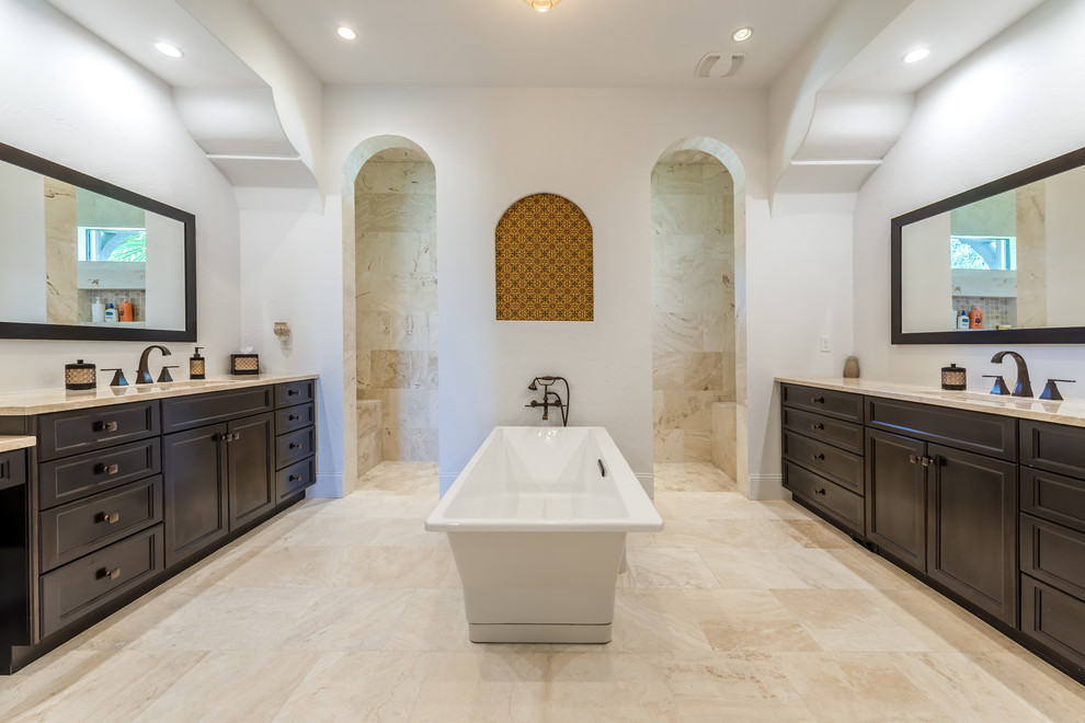 This is an example of a mediterranean master bathroom in Jacksonville with recessed-panel cabinets, dark wood cabinets, a freestanding tub, a curbless shower, beige tile, white walls and an open shower.