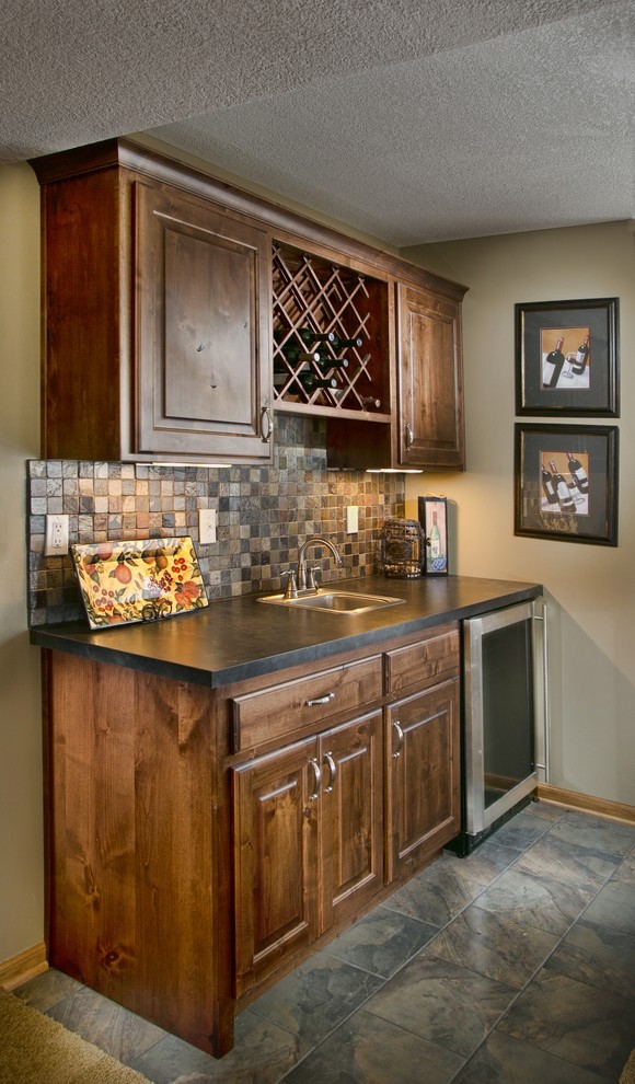 Photo of a mid-sized midcentury single-wall wet bar in Wichita with a drop-in sink, raised-panel cabinets, medium wood cabinets, soapstone benchtops, multi-coloured splashback, stone tile splashback and ceramic floors.