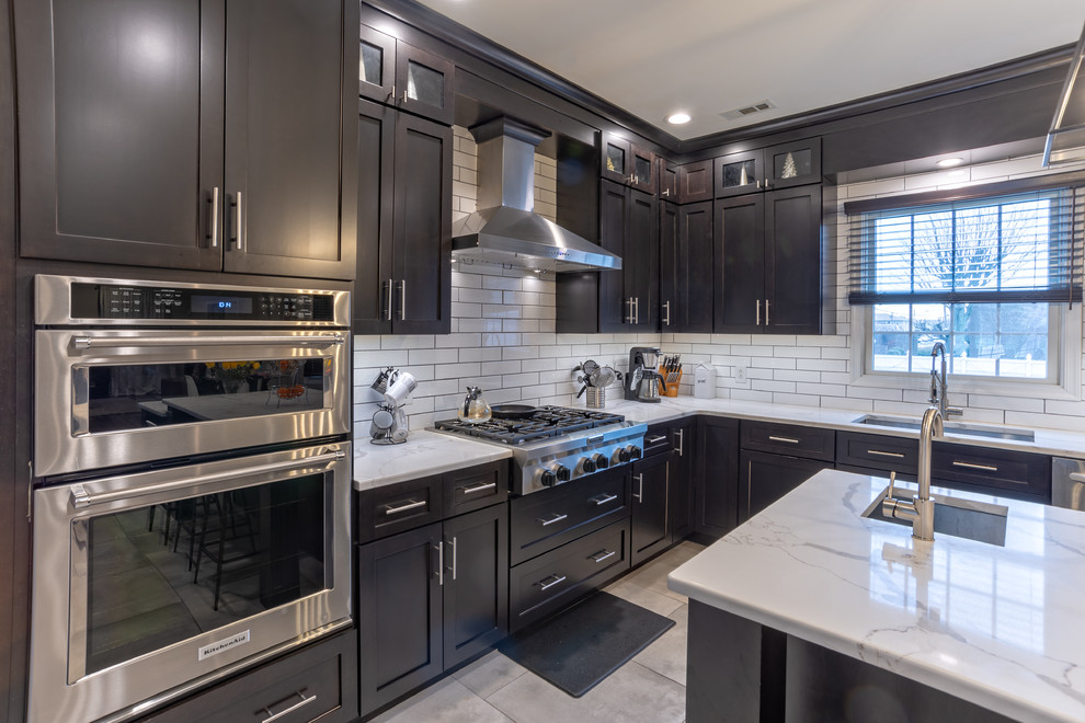 Photo of a large transitional l-shaped eat-in kitchen in Philadelphia with an undermount sink, shaker cabinets, dark wood cabinets, quartz benchtops, white splashback, subway tile splashback, stainless steel appliances, porcelain floors, with island, grey floor and white benchtop.