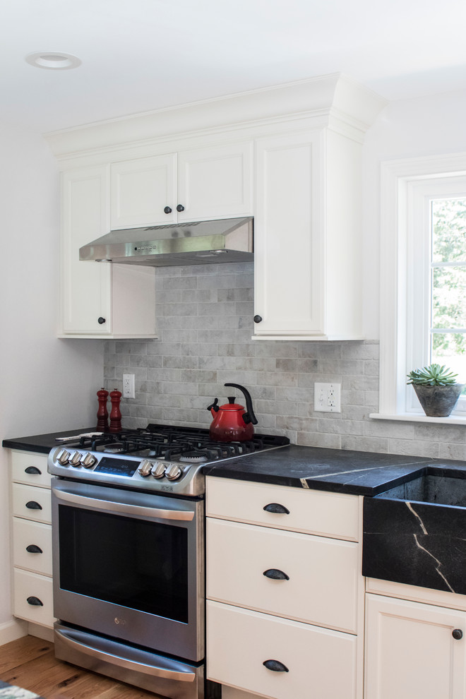 Inspiration for a mid-sized transitional galley open concept kitchen remodel in Boston with a farmhouse sink, recessed-panel cabinets, white cabinets, soapstone countertops, gray backsplash, stainless steel appliances and a peninsula
