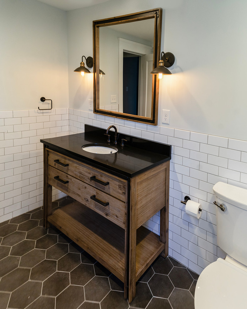 Photo of a mid-sized transitional bathroom in Cincinnati with a curbless shower, white tile, white walls, ceramic floors, an undermount sink, grey floor, a hinged shower door, furniture-like cabinets, a two-piece toilet, ceramic tile, black benchtops, distressed cabinets, a freestanding tub and engineered quartz benchtops.