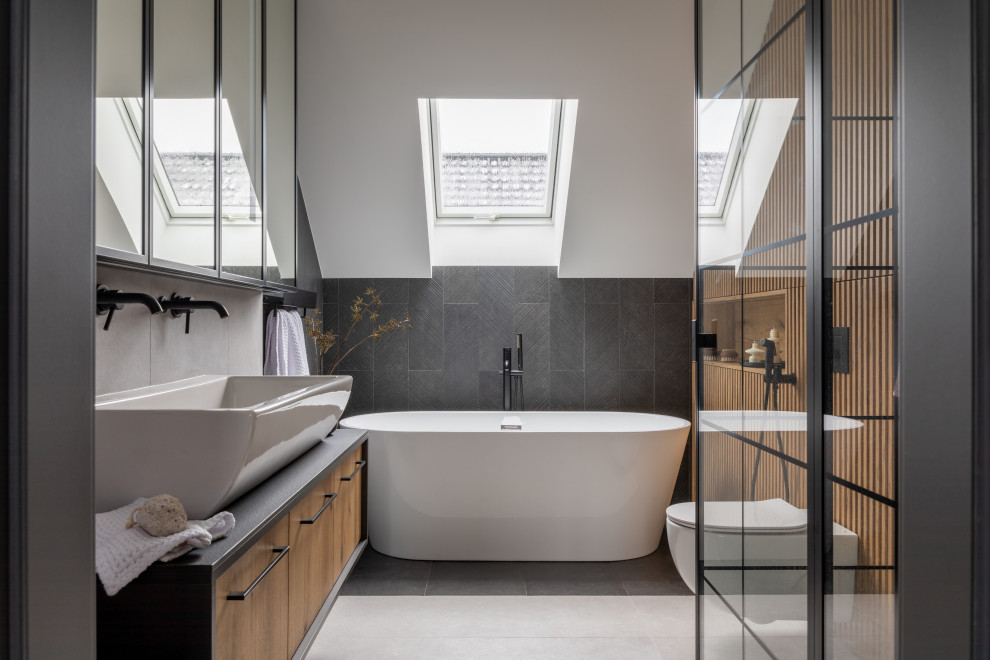 This is an example of a large contemporary master bathroom in San Francisco with recessed-panel cabinets, light wood cabinets, a freestanding tub, an alcove shower, a one-piece toilet, black tile, a vessel sink, concrete benchtops, grey benchtops, a single vanity, a floating vanity, vaulted and wood walls.