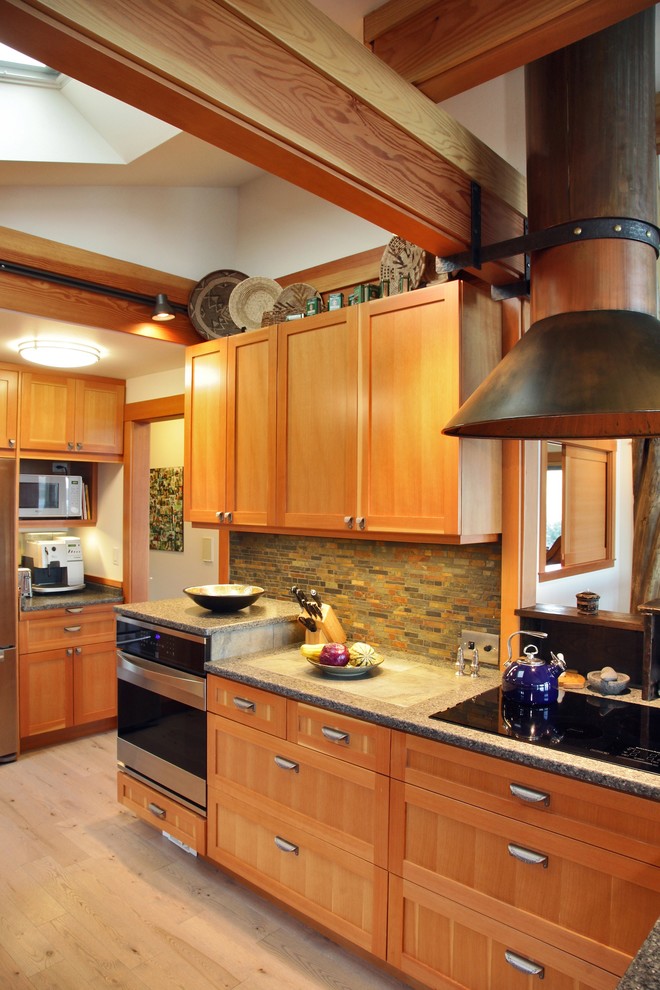 This is an example of a mid-sized eclectic l-shaped open plan kitchen in Seattle with a drop-in sink, shaker cabinets, medium wood cabinets, solid surface benchtops, brown splashback, stone tile splashback and stainless steel appliances.