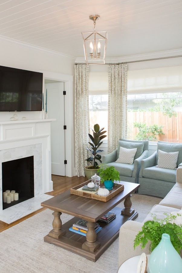 Photo of a mid-sized beach style open concept family room in Santa Barbara with white walls, medium hardwood floors, a standard fireplace, a plaster fireplace surround, a wall-mounted tv and brown floor.