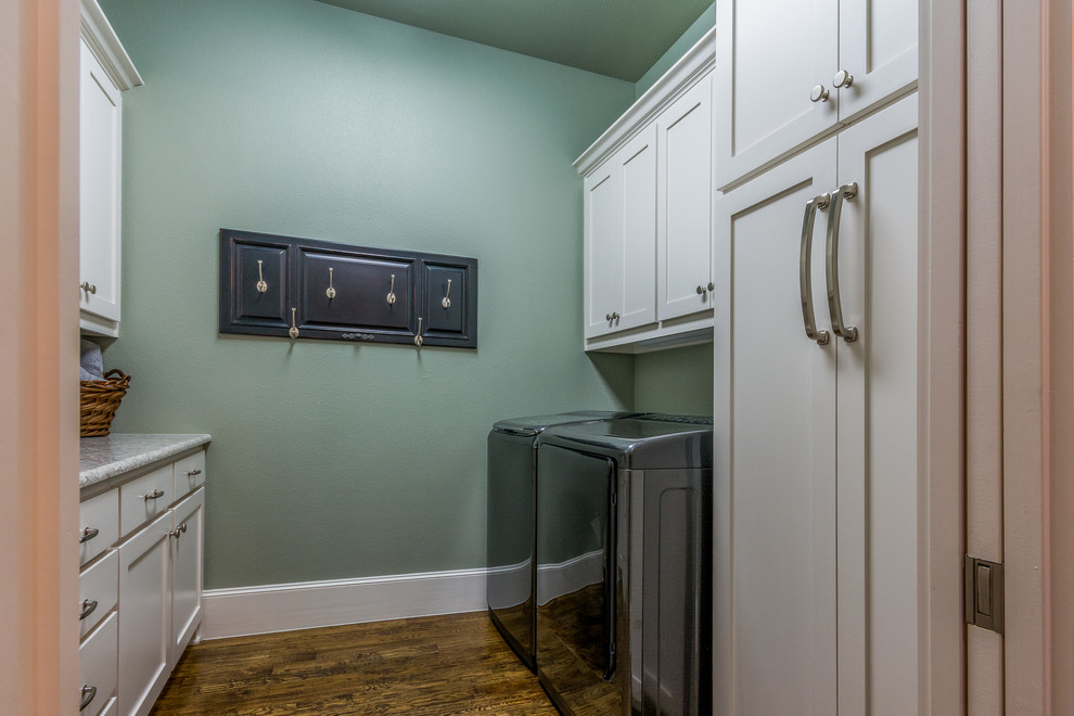 Photo of a large transitional galley dedicated laundry room in Dallas with shaker cabinets, white cabinets, green walls, dark hardwood floors and a side-by-side washer and dryer.