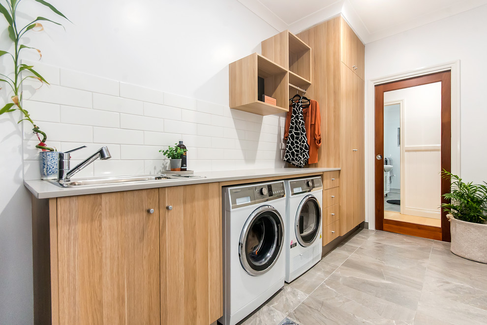 Design ideas for a mid-sized industrial single-wall dedicated laundry room in Other with a drop-in sink, flat-panel cabinets, light wood cabinets, granite benchtops, white splashback, subway tile splashback, white walls, ceramic floors, a side-by-side washer and dryer, grey floor and grey benchtop.