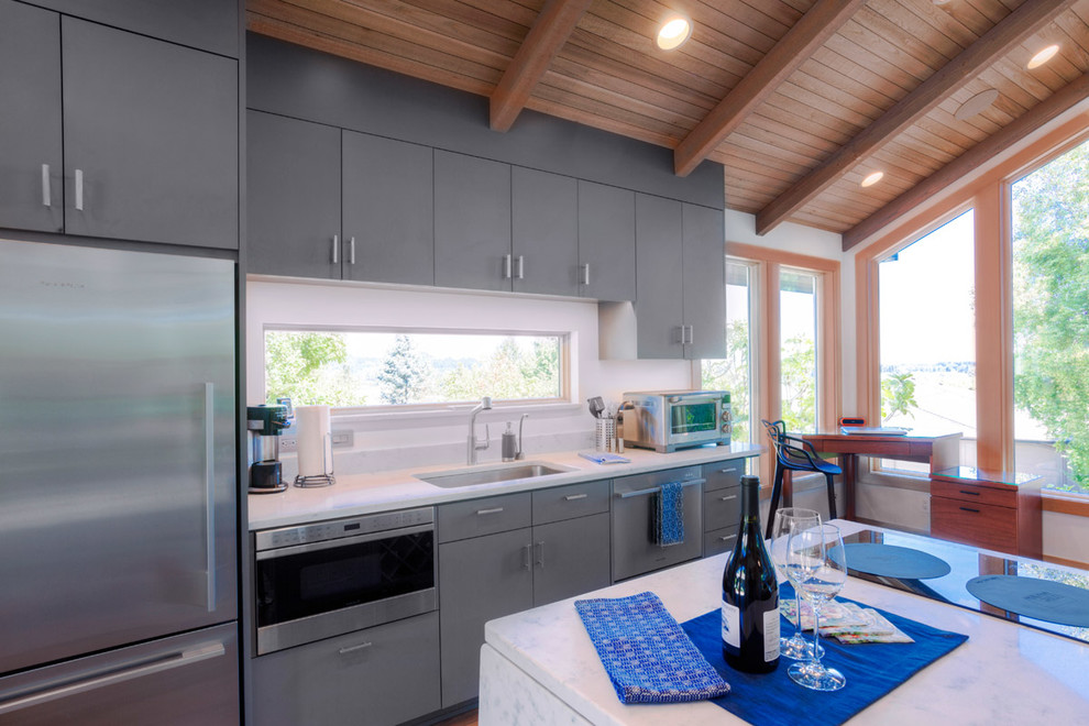 This is an example of a mid-sized transitional galley open plan kitchen in Portland with an undermount sink, flat-panel cabinets, blue cabinets, quartz benchtops, stainless steel appliances, medium hardwood floors and with island.