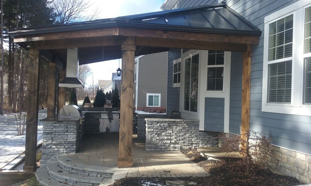 Photo of a mid-sized transitional backyard patio in Columbus with an outdoor kitchen, concrete pavers and a roof extension.