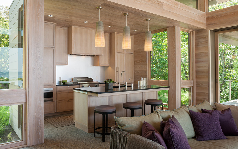 This is an example of a mid-sized contemporary single-wall open plan kitchen in Boston with an undermount sink, flat-panel cabinets, light wood cabinets, soapstone benchtops, panelled appliances, concrete floors, with island and brown floor.