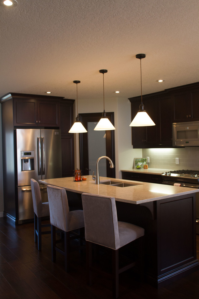 Transitional dark wood floor kitchen photo with an undermount sink, shaker cabinets, dark wood cabinets, quartz countertops, gray backsplash, ceramic backsplash, stainless steel appliances and an island