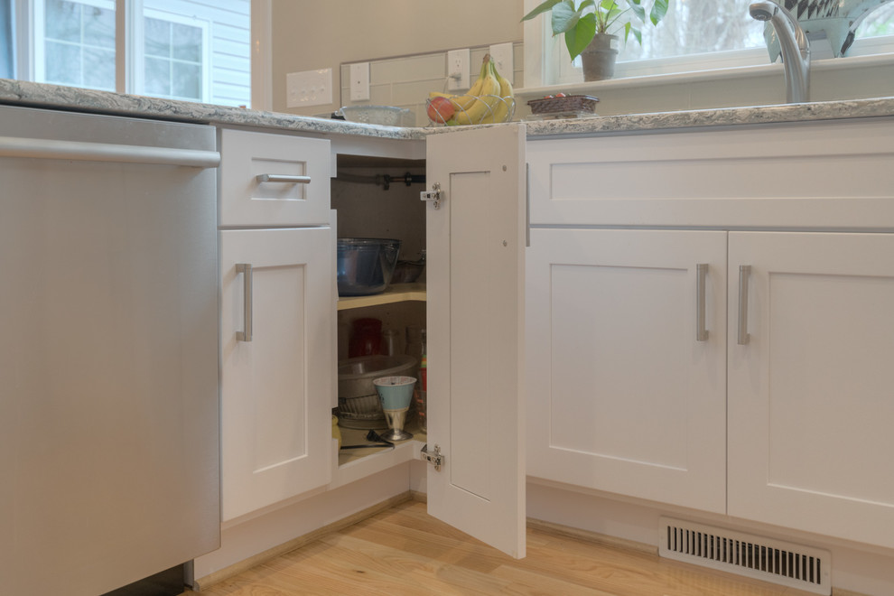 Example of a mid-sized transitional u-shaped light wood floor home design design with an undermount sink, shaker cabinets, white cabinets, quartz countertops, beige backsplash, glass tile backsplash, stainless steel appliances and a peninsula