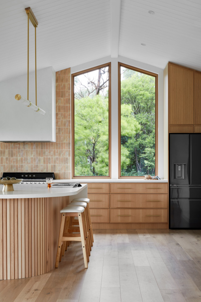 This is an example of a large modern u-shaped open plan kitchen in Melbourne with a double-bowl sink, shaker cabinets, medium wood cabinets, pink splashback, porcelain splashback, black appliances, light hardwood floors, with island, brown floor, white benchtop and exposed beam.