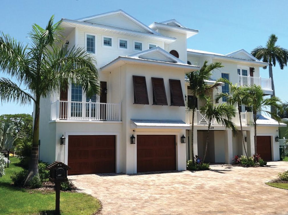 Photo of a large tropical three-storey stucco white house exterior in Tampa with a hip roof and a metal roof.