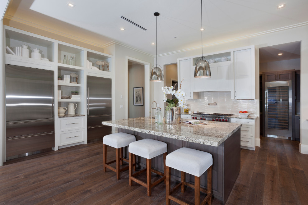 Photo of a large transitional l-shaped kitchen in Miami with an undermount sink, shaker cabinets, white cabinets, white splashback, glass tile splashback, medium hardwood floors, with island, brown floor and brown benchtop.