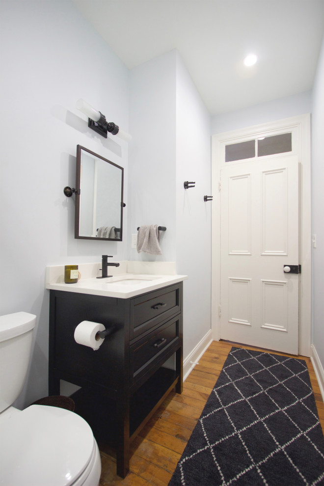 Photo of a small transitional 3/4 bathroom in Other with recessed-panel cabinets, black cabinets, an alcove shower, a two-piece toilet, white tile, ceramic tile, blue walls, medium hardwood floors, an undermount sink, engineered quartz benchtops, a sliding shower screen, white benchtops, a single vanity and a freestanding vanity.