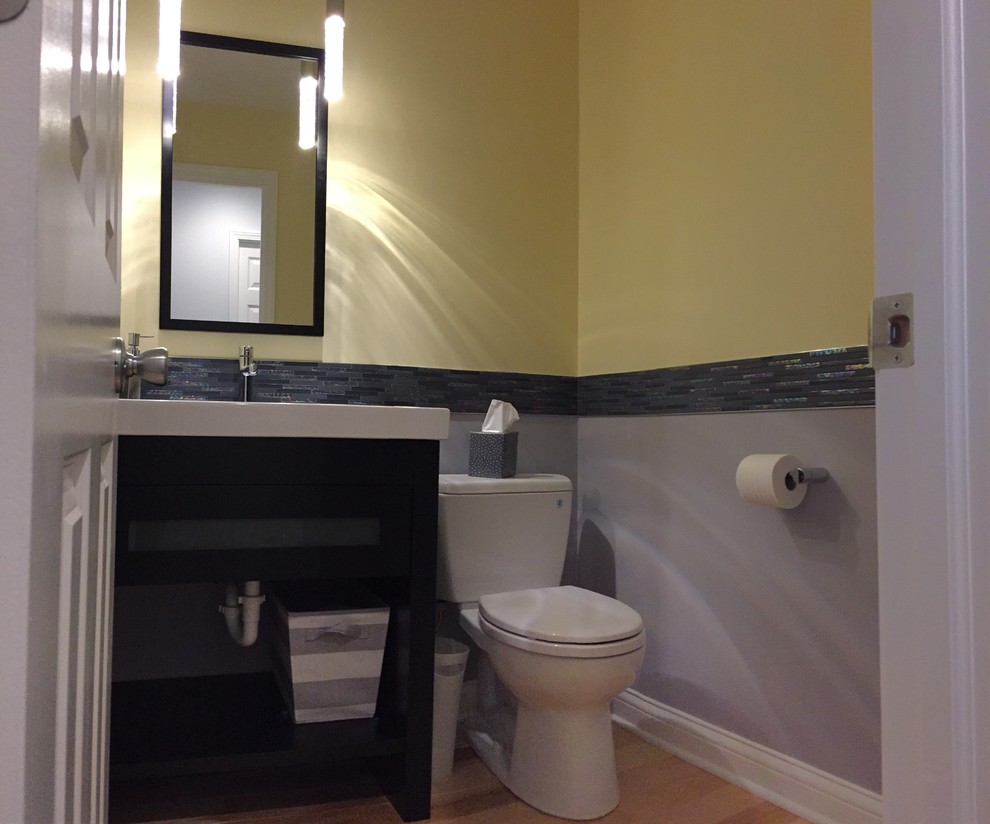 This is an example of a small contemporary 3/4 bathroom in Cleveland with furniture-like cabinets, dark wood cabinets, a two-piece toilet, black tile, glass sheet wall, multi-coloured walls, light hardwood floors, an integrated sink and quartzite benchtops.