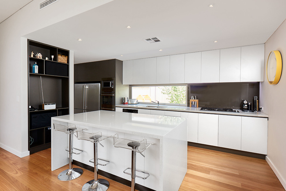 Photo of a mid-sized contemporary single-wall eat-in kitchen in Perth with an undermount sink, open cabinets, white cabinets, solid surface benchtops, brown splashback, stainless steel appliances, light hardwood floors, with island, glass sheet splashback, beige floor and white benchtop.