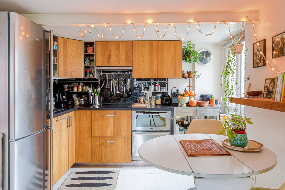 This is an example of an eclectic l-shaped eat-in kitchen in Paris with flat-panel cabinets, medium wood cabinets, black splashback, stainless steel appliances, no island, white floor and black benchtop.