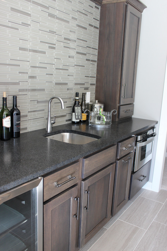 Photo of a mid-sized transitional single-wall wet bar in Other with an undermount sink, flat-panel cabinets, grey cabinets, granite benchtops, multi-coloured splashback, mosaic tile splashback, ceramic floors, grey floor and black benchtop.