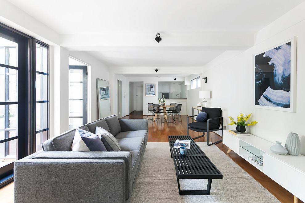 Contemporary formal open concept living room in Melbourne with white walls, medium hardwood floors and brown floor.