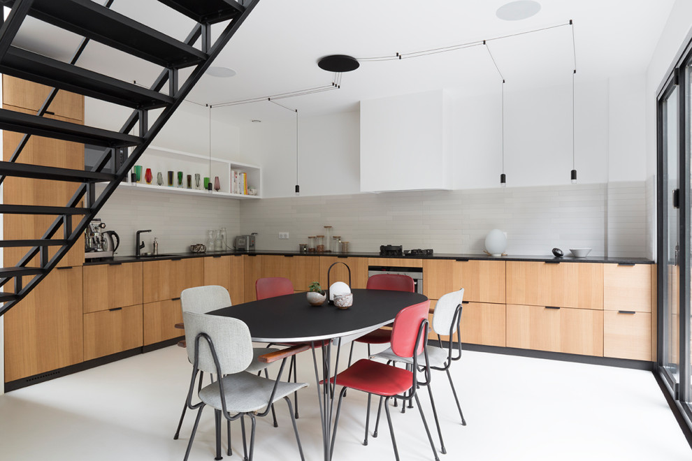 This is an example of a large contemporary l-shaped eat-in kitchen in Paris with an undermount sink, flat-panel cabinets, beige cabinets, grey splashback, ceramic splashback, panelled appliances, concrete floors, no island, white floor and black benchtop.