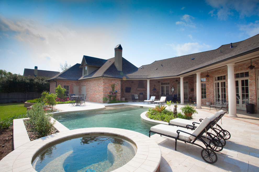 Mid-sized traditional backyard custom-shaped pool in New Orleans with natural stone pavers and a hot tub.