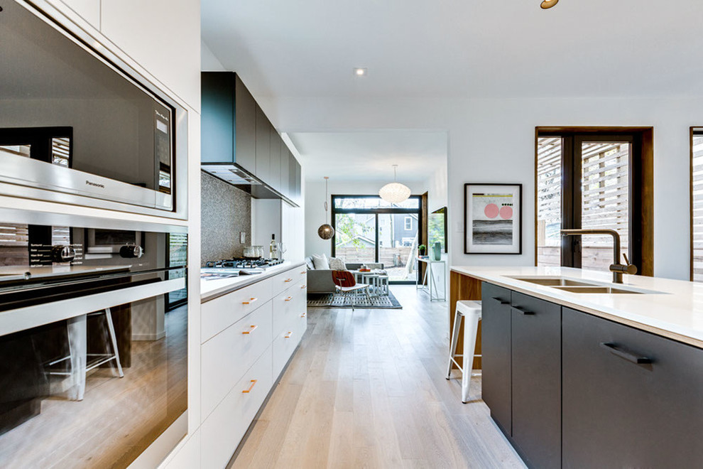 Inspiration for a mid-sized contemporary eat-in kitchen in Toronto with a double-bowl sink, flat-panel cabinets, black cabinets, quartz benchtops, multi-coloured splashback, mosaic tile splashback, panelled appliances, light hardwood floors and with island.
