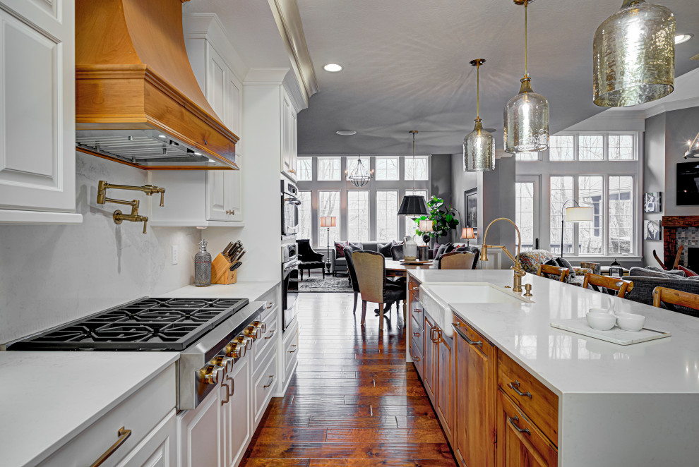Modern inredning av ett mellanstort vit vitt kök, med en rustik diskho, luckor med upphöjd panel, vita skåp, bänkskiva i kvarts, vitt stänkskydd, rostfria vitvaror, mellanmörkt trägolv, en köksö och brunt golv