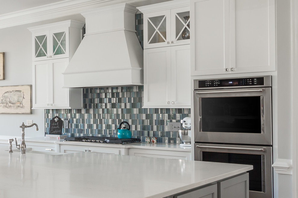 Open concept kitchen - large transitional l-shaped medium tone wood floor open concept kitchen idea in Raleigh with a farmhouse sink, flat-panel cabinets, white cabinets, quartz countertops, blue backsplash, glass tile backsplash, stainless steel appliances and an island