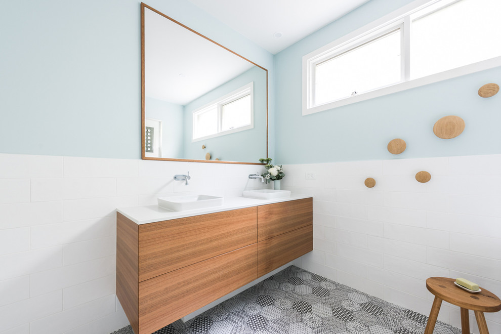 Photo of a mid-sized contemporary master bathroom in Melbourne with flat-panel cabinets, medium wood cabinets, a freestanding tub, an alcove shower, a one-piece toilet, white tile, porcelain tile, blue walls, porcelain floors, a drop-in sink, engineered quartz benchtops, multi-coloured floor, a hinged shower door and white benchtops.
